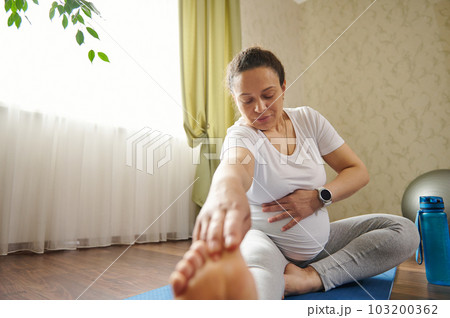 African ethnic charming womanadult gravid pregnant woman holding hand on her belly, doing prenatal stretching exercises on fitness mat. Yoga practice and meditation. Healthy pregnancy. Front shot 103200362