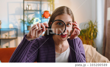 Woman hold magnifying glass near face, looking into camera with big zoomed eye, searching, analysing Woman hold magnifying glass near face, looking into camera with big zoomed eye, searching, analysing 103200589