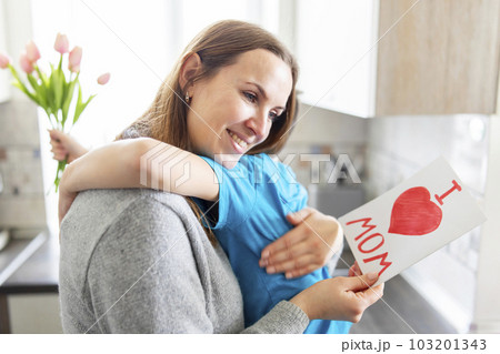 Boy congratulating his mom and giving her flowers tulips and greeting card 103201343