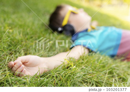 Happy boy in sunglasses lying on the grass and listening to music in headphones 103201377