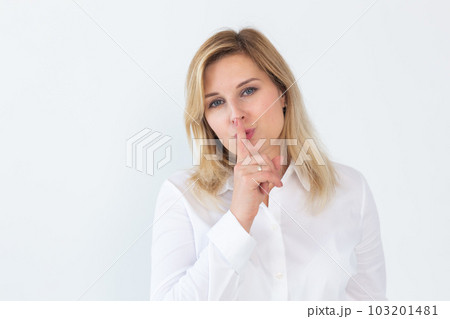 Beautiful young Caucasian woman isolated on white studio background hold finger at lips ask be silent quiet. Millennial female look at camera tell share mystery, announce secret sale or discount 103201481