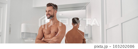 Positive man with towel and crossed arms leans onto cabinet near mirrror in bathroom Positive man with towel and crossed arms leans onto cabinet near mirrror in bathroom 103202086