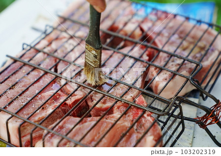 Meat steaks are greased with vegetable oil on grill rack. Cooking over open fire 103202319