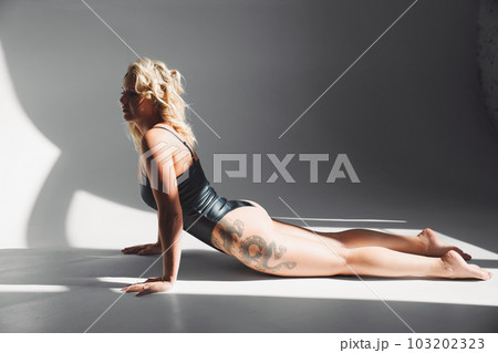 a sexy blonde with tattoos in a leather swimsuit performs sports exercises a sexy blonde with tattoos in a leather swimsuit performs sports exercises 103202323