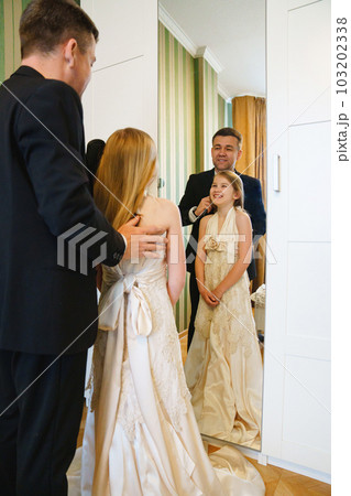 dad and little blonde teenage girl in her mother's wedding dress by the mirror. 103202338