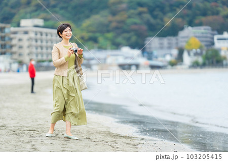 海辺で写真を撮るミドル女性 103205415