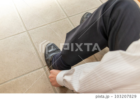 玄関で屈んで靴を履く男性 103207829