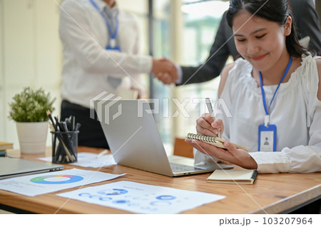 A young Asian female assistant taking notes on her spiral notepad during the meeting. 103207964