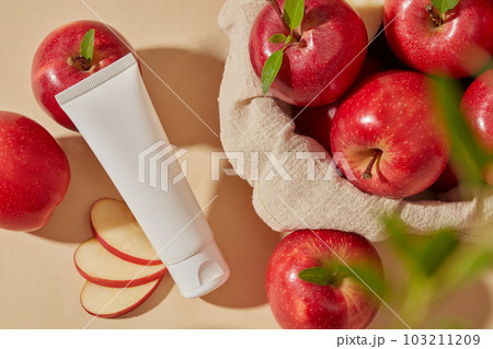 A basket cover with towel and filled with several fresh apples. Unlabeled cosmetic container for branding mockup of Apple (Malus domestica) extract 103211209