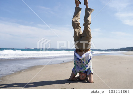波打ち際でヘッドスタンドをするサングラスの男性 波打ち際でヘッドスタンドをするサングラスの男性 103211862