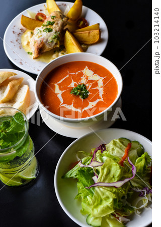 Lunch set made of tomato cream soup, salad, chicken with potato, lemonade on black background 103214140