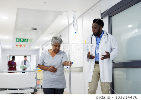 African american male doctor talking to diverse senior female patient holding drip stand in corridor African american male doctor talking to diverse senior female patient holding drip stand in corridor 103214476