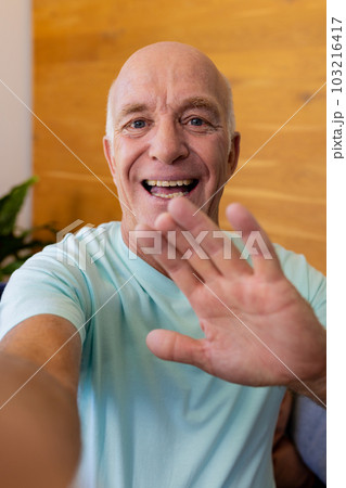 Happy senior caucasian man making video call smiling and waving at home Happy senior caucasian man making video call smiling and waving at home 103216417