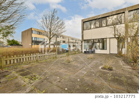 an empty parking area in front of a building with trees and bushes on either side, there is a blue sky 103217775