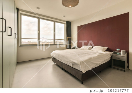 a bedroom with a large bed and red accent on the wall behind it is a window that looks out onto the street 103217777