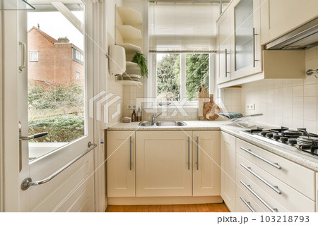 a kitchen with wood flooring and white cabinetd cupboards on either side of the window looking out onto the street 103218793