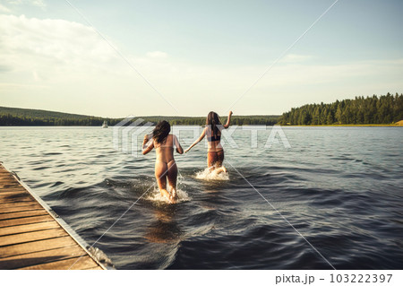 Two young women splashing in the water on a wooden pier. Generative AI 103222397