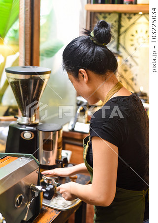 Vietnamese waitress making coffee via portafilter of a coffee machine 103225034