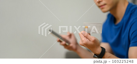 Man hand holding credit card and using smartphone for making online transactions or checking her bank account 103225248