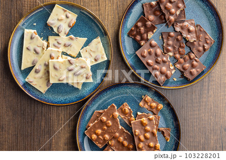 Broken chocolate bars with nuts on wooden table. Top view. Broken chocolate bars with nuts on wooden table. Top view. 103228201