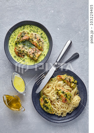 Chkmeruli on a dark plate with cutlery and gravy boats with oill and milk cream. Plate of spaghetti with fried chicken 103229405