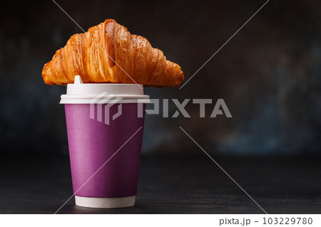 Aromatic coffee in a paper cup paired with a flaky croissant Aromatic coffee in a paper cup paired with a flaky croissant 103229780