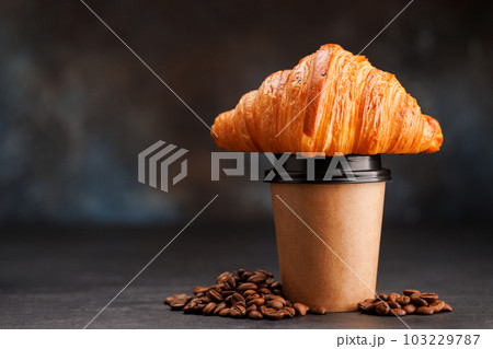 Aromatic coffee in a paper cup paired with a flaky croissant Aromatic coffee in a paper cup paired with a flaky croissant 103229787