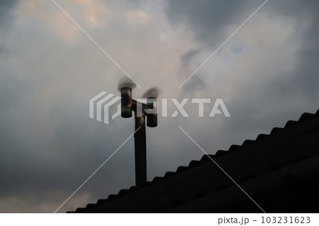 A silhouette of a black tube and smokestacks against a toxic smog-filled sky. The energy industry's technology and construction rely on oil, contributing to harmful plant emissions. Out of focus 103231623