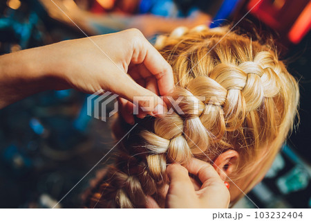 Process of braiding the master weaves braids on her head blond little girl in beauty salon close up. Professional hair care and creating hairstyles. 103232404