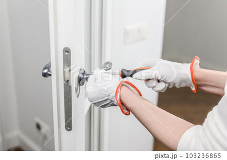 A man fixes a door with a screwdriver. Door lock repair A man fixes a door with a screwdriver. Door lock repair 103236865