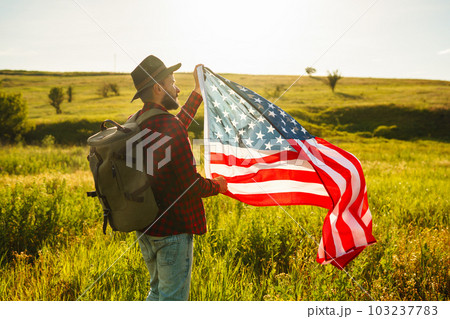 4th of July. American Flag. Traveler with the flag of America. The man in a hat, a backpack, a shirt and jeans. 103237783