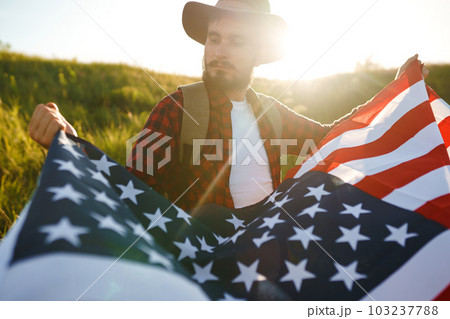 4th of July. American Flag. Traveler with the flag of America. The man in a hat, a backpack, a shirt and jeans. 4th of July. American Flag. Traveler with the flag of America. The man in a hat, a backpack, a shirt and jeans. 103237788