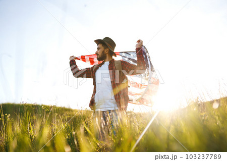 4th of July. American Flag. Traveler with the flag of America. The man in a hat, a backpack, a shirt and jeans. 4th of July. American Flag. Traveler with the flag of America. The man in a hat, a backpack, a shirt and jeans. 103237789