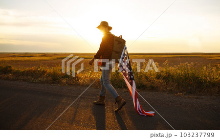 4th of July. American Flag. Traveler with the flag of America. The man in a hat, a backpack, a shirt and jeans. 4th of July. American Flag. Traveler with the flag of America. The man in a hat, a backpack, a shirt and jeans. 103237799