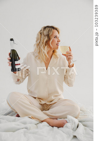 blonde in delicate pajamas in bed with a bottle and a glass of champagne blonde in delicate pajamas in bed with a bottle and a glass of champagne 103239389