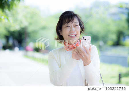 屋外でスマートフォンを操作するシニア女性の手元 103241756