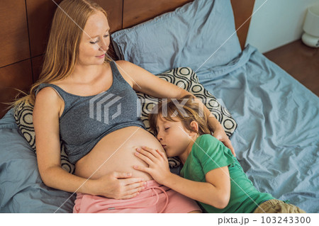 Young beautiful pregnant woman and eldest son. The cute boy leaned his ear against his mother's belly. Expecting a baby in the family concept. Preparing an older child for a younger one Young beautiful pregnant woman and eldest son. The cute boy leaned his ear against his mother's belly. Expecting a baby in the family concept. Preparing an older child for a younger one 103243300