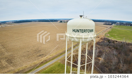 Drone aerial of empty field, partial forest in winter and green grass with Huntertown city water tower in Midwest America 103244364