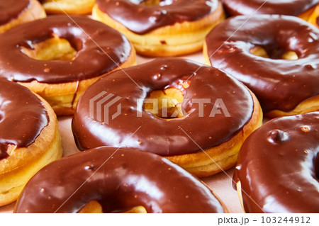 Side shot of half glazed yeast donuts with chocolate frosting on white tray background Side shot of half glazed yeast donuts with chocolate frosting on white tray background 103244912