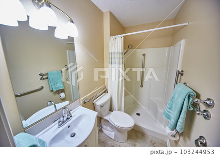 Clean white and beige handicap bathroom with built in railing and shower seating teal blue towel 103244953