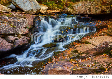 Small cascading river with rocks covered in fall leaves and tiny rock stack by edge Small cascading river with rocks covered in fall leaves and tiny rock stack by edge 103245415