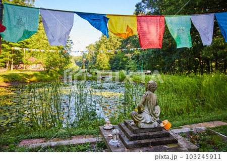 Lily pond from behind Tibetan Mongolian Buddhist statue with prayer flags overhead Lily pond from behind Tibetan Mongolian Buddhist statue with prayer flags overhead 103245911
