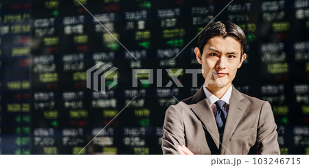 電光掲示板の株価ボードの前で腕組みをするカメラ目線の男性 103246715