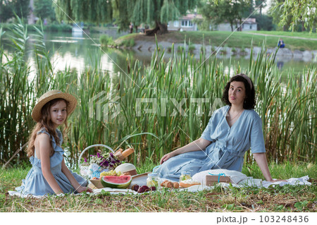 A mother and daughter on a picnic in a park on the banks of a river A mother and daughter on a picnic in a park on the banks of a river 103248436