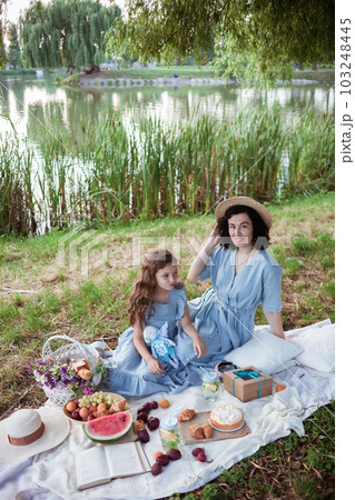 A mother and daughter on a picnic in a park on the banks of a river A mother and daughter on a picnic in a park on the banks of a river 103248445