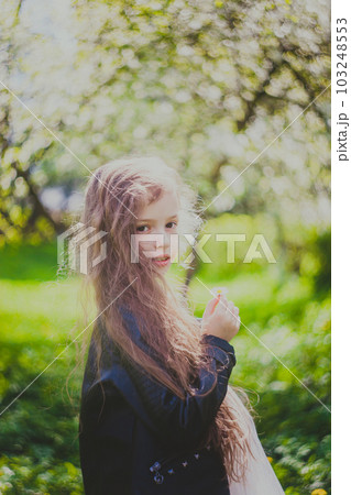 Little girl in black jacket standing in the spring cherry garden 103248553