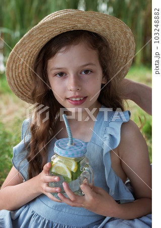 A young lady drinks lemonade on a picnic in a park on the banks of a river A young lady drinks lemonade on a picnic in a park on the banks of a river 103248882