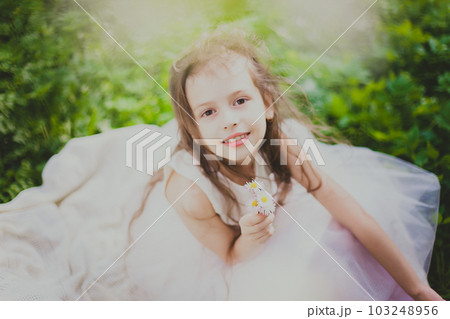 A girl in dress sniffs a bouquet of daisies in spring cherry garden A girl in dress sniffs a bouquet of daisies in spring cherry garden 103248956