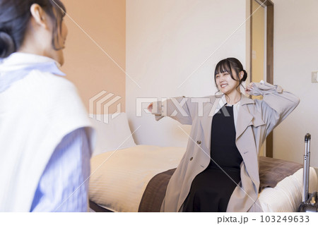 チェックインして客室のベッドに座って伸びをする若い女性　旅行、出張イメージ 103249633