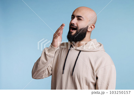 Young arab man looking sleepy and exhausted while yawning. Tired person with bored facial expression feeling sleepiness while covering mouth with hand and posing in studio Young arab man looking sleepy and exhausted while yawning. Tired person with bored facial expression feeling sleepiness while covering mouth with hand and posing in studio 103250157